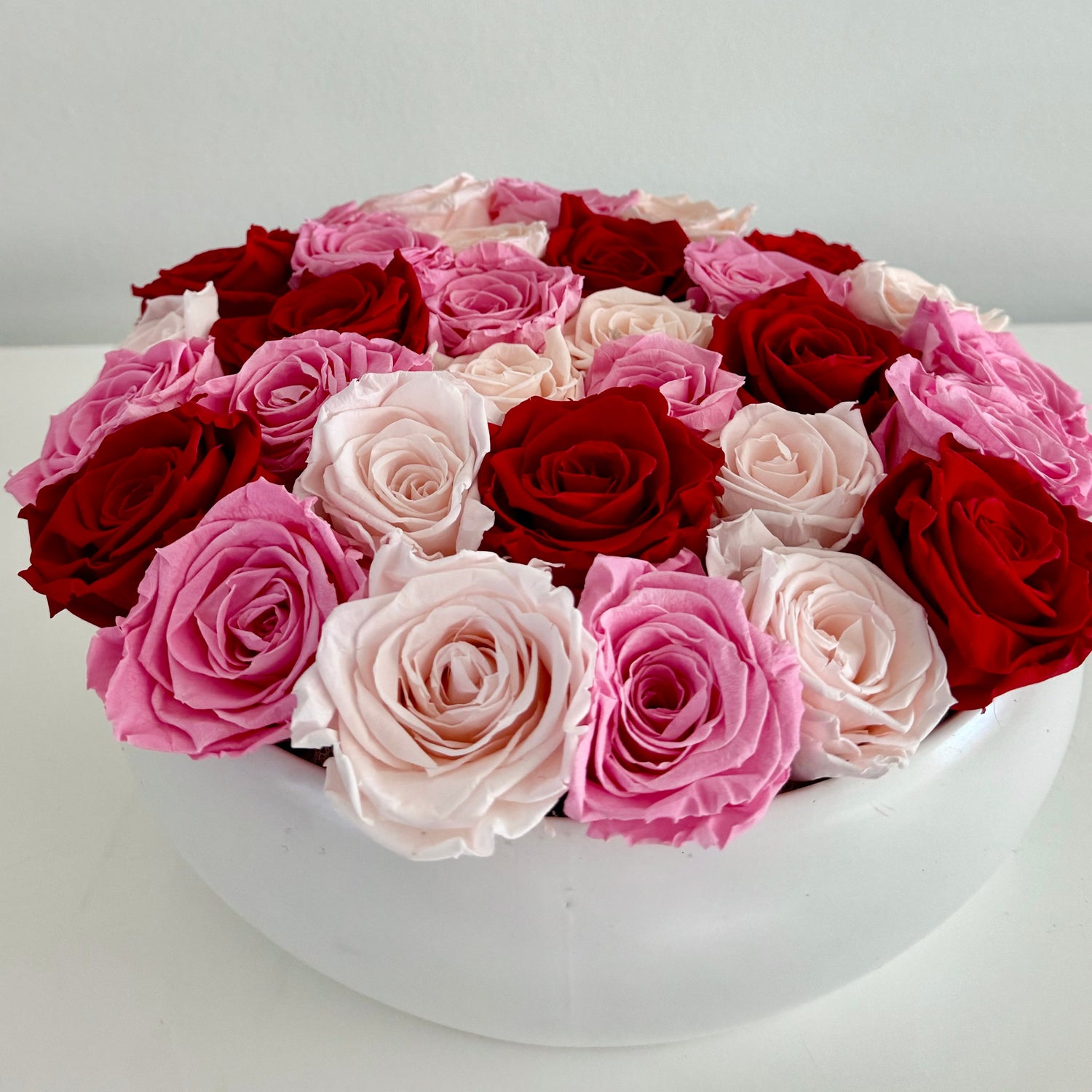 Red, hot pink and blush roses packed tightly into a round white bowl.